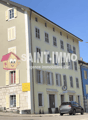A multi-story building with a cartoon character on the side, yellow shutters, and a sign for an agency. A car is parked in front.