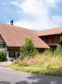 Traditional wooden house, brown roof, green windows, white walls, chimney, balcony