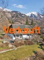 Detached house, white exterior, gray roof, surrounded by trees, mountains in the background, driveway