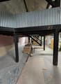 interior of a building, raised ground floor, corrugated metal roof, metal support beams, concrete floor, stack of wooden planks