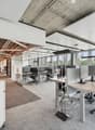 Modern office layout, desks, chairs, white walls, ceiling panels, windows, carpeted floor, exterior view, bookshelves, pink storage bin.
