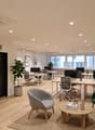 modern office space with wooden floors, white walls, multiple desks, office chairs, plants, bookshelves, and a rug