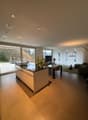modern kitchen with central island, balcony with seating, large glass windows, dining table, green area with table, couch, television, large floor lamp
