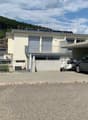 white house, concrete garage, cars parked, solar panels on the roof, fenced yard, mountains in the background
