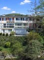 3 story apartment building, white exterior, red shutters, balconies, garage, garden, river view