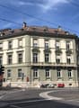 corner building, multiple stories, green color, balcony, windows, traffic lights, people, motorcycles