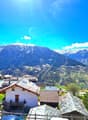 Mountain village with several houses, snow-capped mountains, green fields, clear blue sky