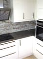 Modern kitchen with white cabinets, black countertops, stone backsplash, built-in oven and dishwasher