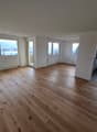 Spacious open-plan living area with large windows, hardwood flooring, and a view of the city outside. The room appears to be a living room or combined living/dining area.