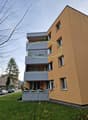 3-story apartment building with beige paint, balcony, glass windows, outdoor plant boxes