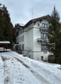 Two story building, snow covered ground, white building, wooden awning, balcony, attached garage