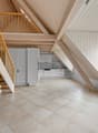 A room with wooden beams, tiled floor, white cabinets, and a staircase.