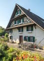 2 story house, white exterior, green shutters, brown roof, garden, seating area, table and chairs