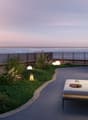 Outdoor lounge area with couch, decorative lamps, grass, and sea view.