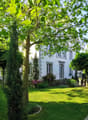 2 story house, white exterior, surrounded by green lawn, flower garden, trees, pathway