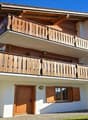 Two story house, wooden balcony, red roof, two doors, one window, garden