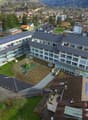 A multi-story school building with a large courtyard and parking area, surrounded by a residential neighborhood in a mountainous area.