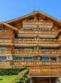 wooden chalet, multiple balconies, flower boxes, surrounded by trees and greenery