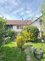 well-maintained garden with various plants, trees, shrubs, pathway, metal arch, patio set, metal trellis, and a house in the background