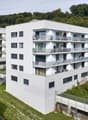 White apartment building, multiple balconies, multiple windows, surrounded by green landscape