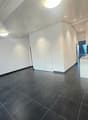 Empty room with white walls, black tiled floor, white ceiling, two doors, kitchen area with countertop and cabinets