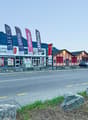 A commercial building with a car parked outside, flags on poles, large windows, red doors, mountains in the background.