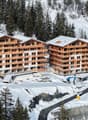 Two wooden apartment buildings, multiple floors, balconies, snow-covered surroundings, under construction