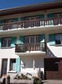 white house, 3 floors, turquoise shutters, brown garage door, balcony on each floor