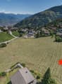 large open field for construction, surrounded by alpine houses and greenery, mountainous backdrop