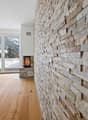 Spacious living room with a stone fireplace, large windows overlooking a snowy landscape, and hardwood flooring.