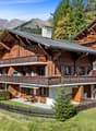 large chalet, wooden exterior, balcony, lawn, terrace, surrounded by trees