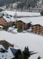 Building complex with multiple apartment buildings with snow on the ground and surrounding mountains.