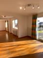 Large living room, hardwood floor, ceiling lights, large windows with curtains, sliding doors to balcony