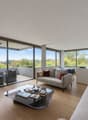 large sliding glass doors leading to a balcony, hardwood floors, large windows with scenic view, modern grey sofa, coffee table, flatscreen TV on stand, minimalist decor