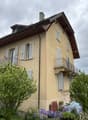 2 story house, beige paint, several windows, balcony on second floor, small front garden