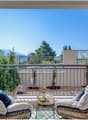 two wicker chairs with cushions, small table with wine bottle and grapes, railings, sunny view of mountains