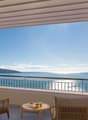 Spacious balcony with panoramic view of the sea, mountains, and blue sky. Furnished with comfortable wicker chairs and a small table, providing an ideal spot to relax and enjoy the scenic surroundings.