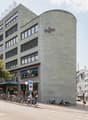 Regus building, multiple floors, glass windows, bicycles parked outside, trees, cars parked on the street