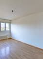 Empty room with white walls, wooden floor, large window, heater