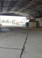 empty warehouse with concrete floor, metal roofing, large open space, some equipment, brick walls, windows, door on the right side
