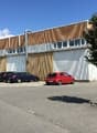Industrial building with multiple windows, cars parked in front, tree in front