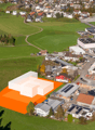 Proposed building outlined on a green field, with many houses and buildings in the background, a few solar panels installed.