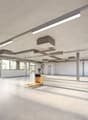 Large open commercial space with concrete floors, exposed ceiling, and overhead lighting. The space has large windows providing natural light and a forklift visible, indicating it may be used for storage or distribution purposes.