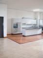 Spacious open-plan kitchen with white cabinets, built-in appliances, and hardwood flooring. Large windows provide natural light. Metal staircase visible in the background.
