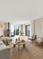 ample living room with sofa, chairs, coffee table, plants, fireplace, glass windows with curtains, balcony, carpet, lamp