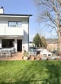 2 story house, white exterior, large windows, balcony, outdoor dining area, garden, trees, lawn