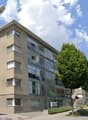 4 story building, glass windows, beige exterior, street light, trees, cars parked