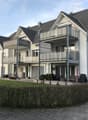 3 story apartment building, white exterior, gray roof, multiple balconies, garden, paved walkway