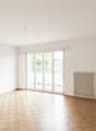 large room with white walls, wooden floor, sliding glass doors leading to a balcony, white radiator