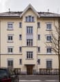 4 story building, beige walls, white windows, brown door, car parked in front
